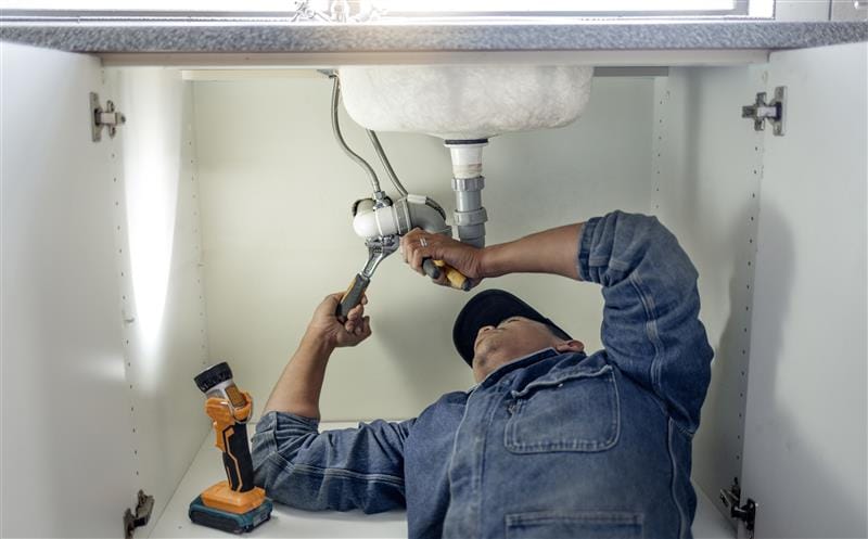 Plumber repairing pipes beneath a bathroom sink in Davis